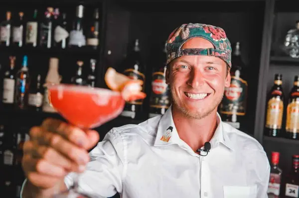 Smilende bartender byder på en rød cocktail